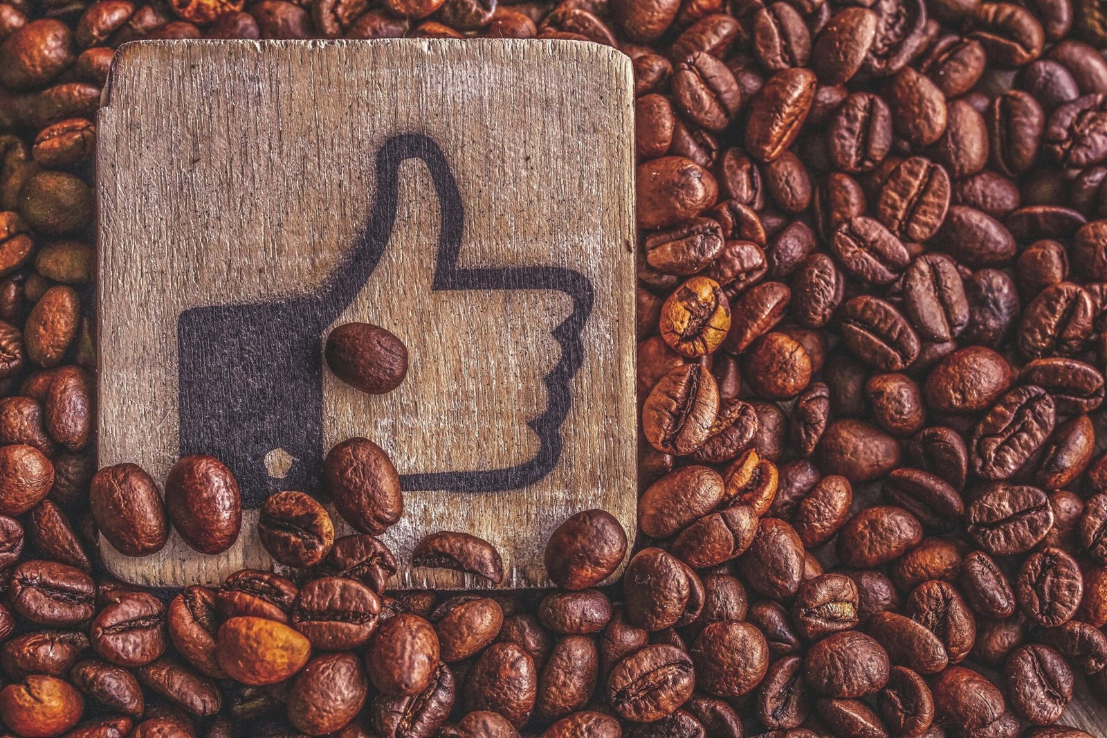A wooden thumbs up symbol resting on a pile of roasted coffee beans, representing appreciation.